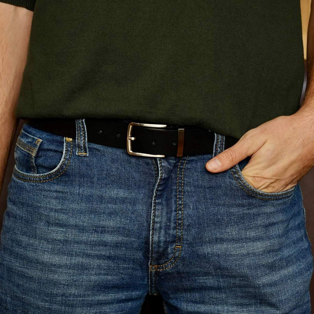 Person wearing a black belt with a shiny buckle on blue jeans.