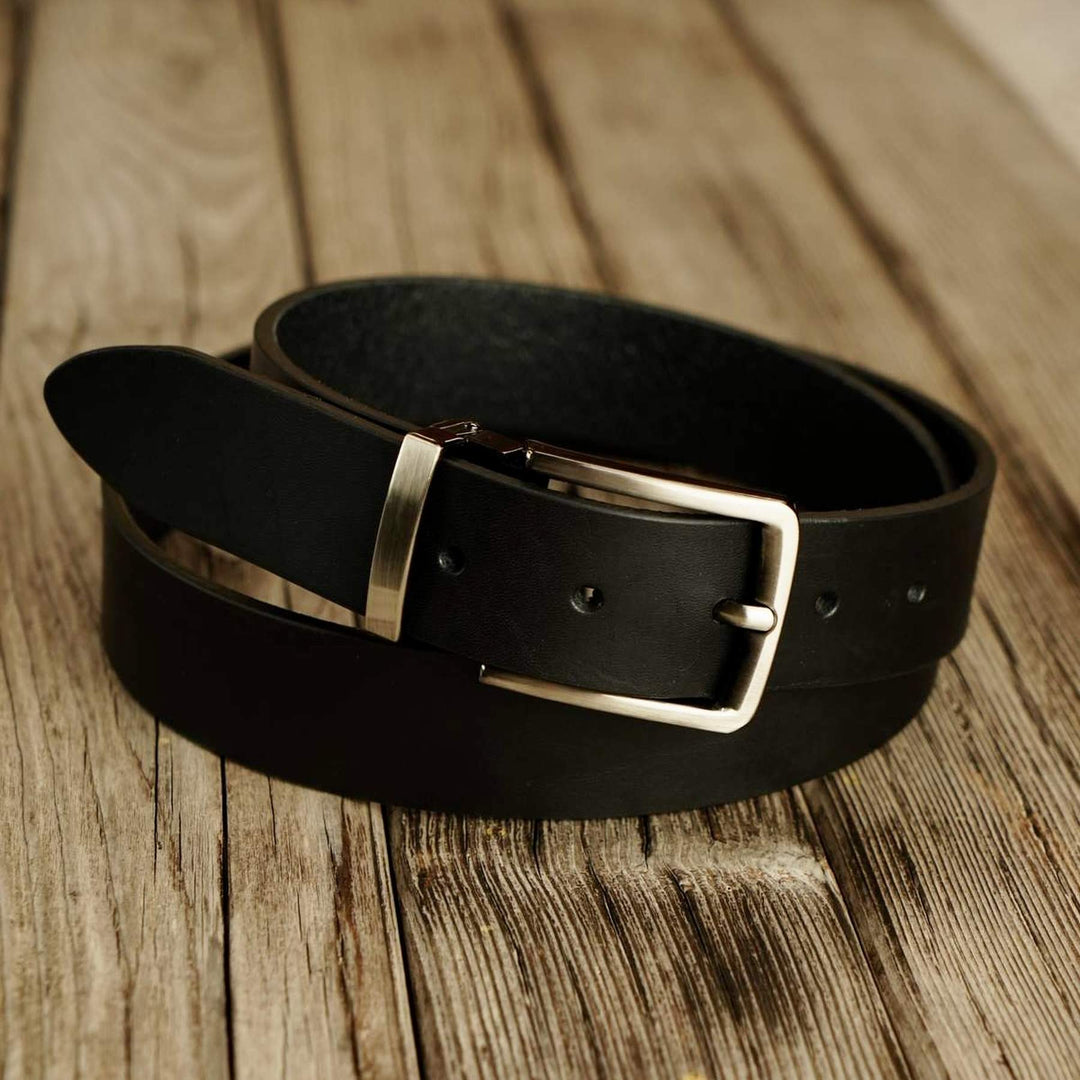 Black leather belt with a buckle on a wooden surface