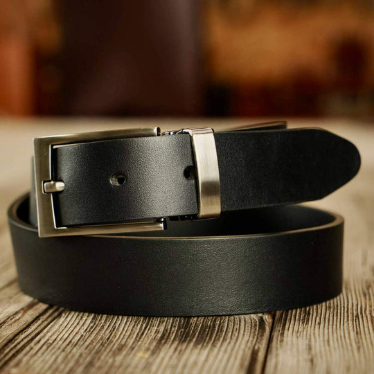 Black leather belt with a silver buckle on a wooden surface