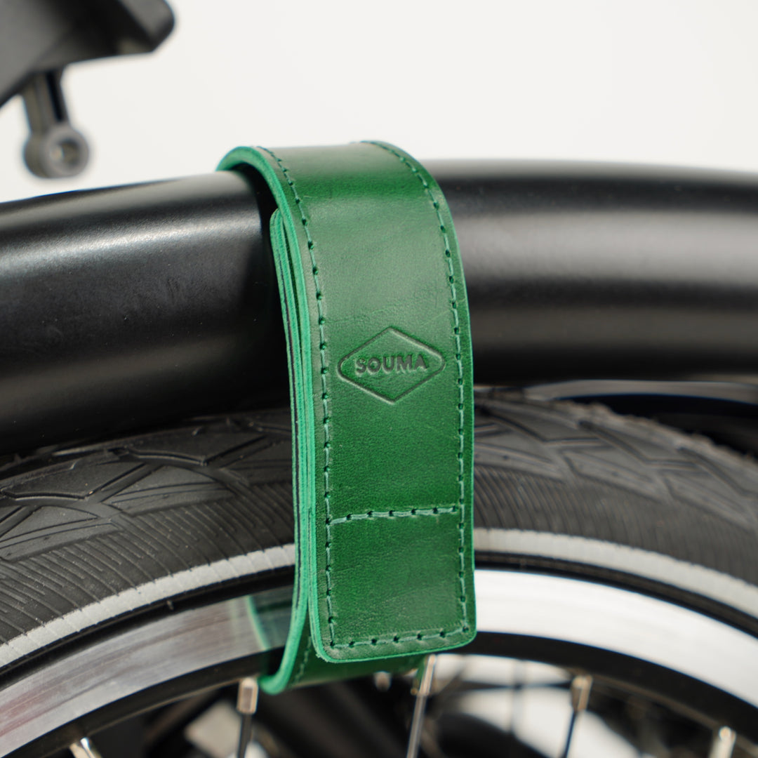 Leather Brompton Wheel Frame strap and Trouser Strap, pants strap, green colour on folded black Brompton bike, detail with Souma Leather logo rotated