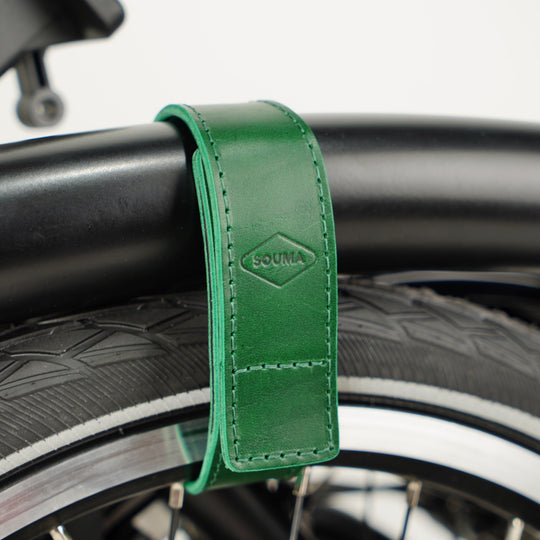 Leather Brompton Wheel Frame strap and Trouser Strap, pants strap, green colour on folded black Brompton bike, detail with Souma Leather logo rotated