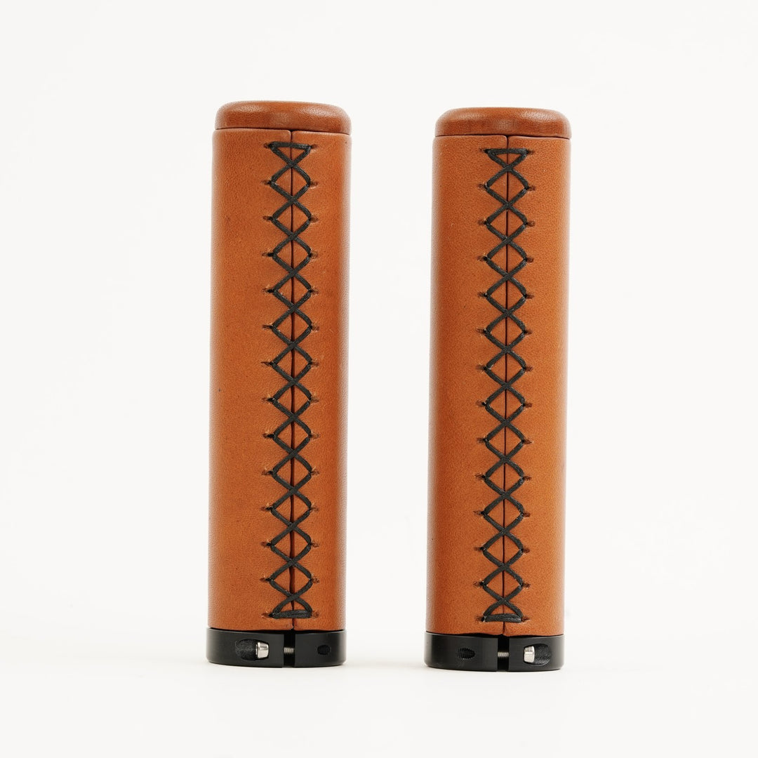 Two honey leather grips with black stitching on a white background