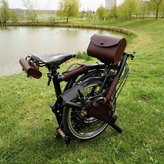 Brompton bicycle with brown leather front carrier bag parked on grass near a pond