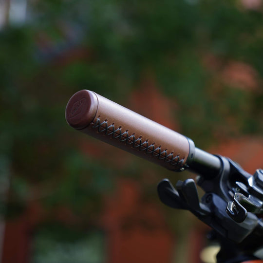 Close-up of a brown leather handlebar grip stitching on a blurred natural background