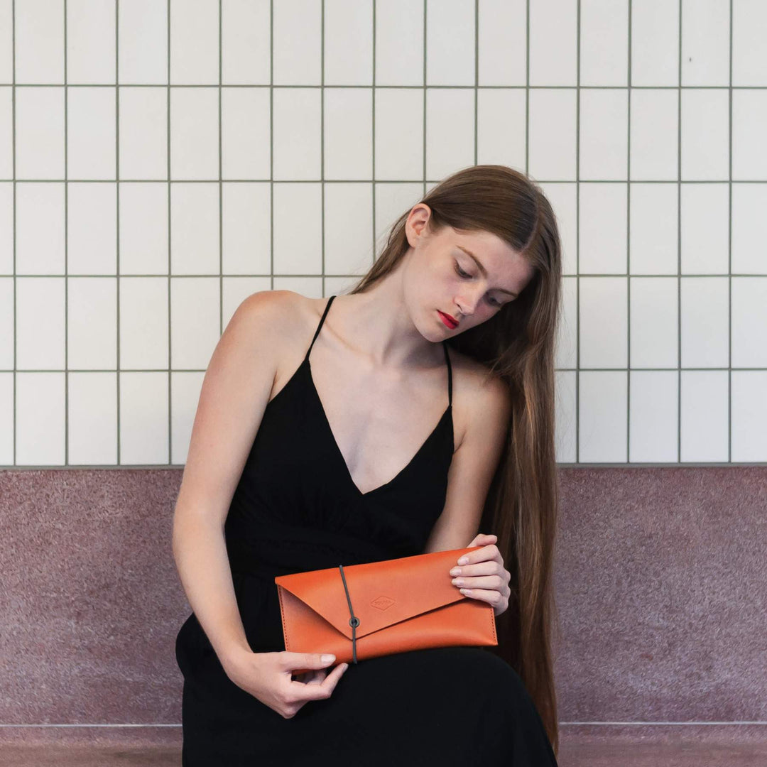 Woman holding an cognac clutch against a tiled wall background