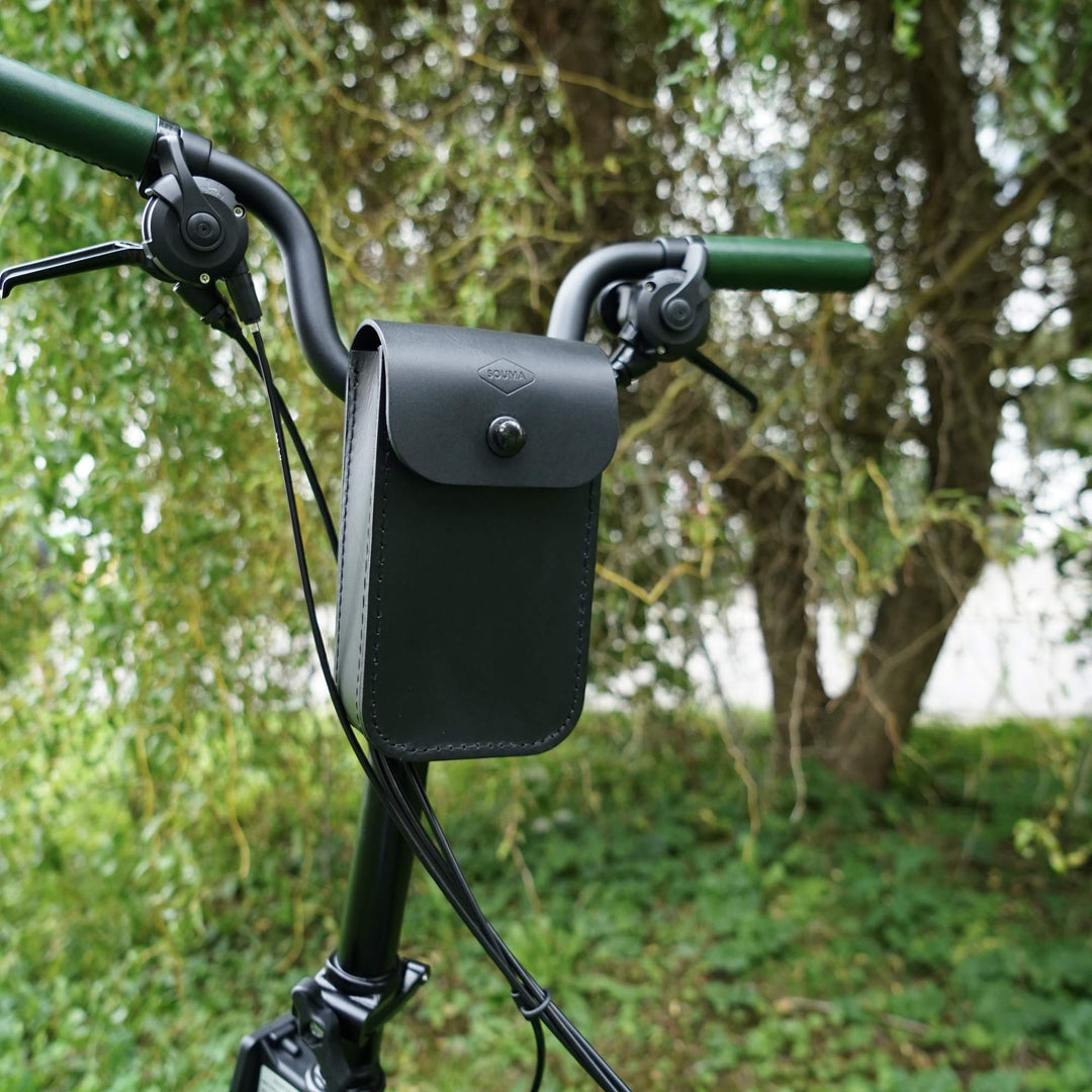 Black leather bag attached to a bicycle handlebar with a blurred green outdoor background