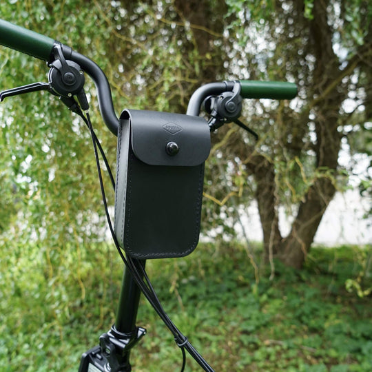 Black leather bag attached to a bicycle handlebar with a blurred green outdoor background