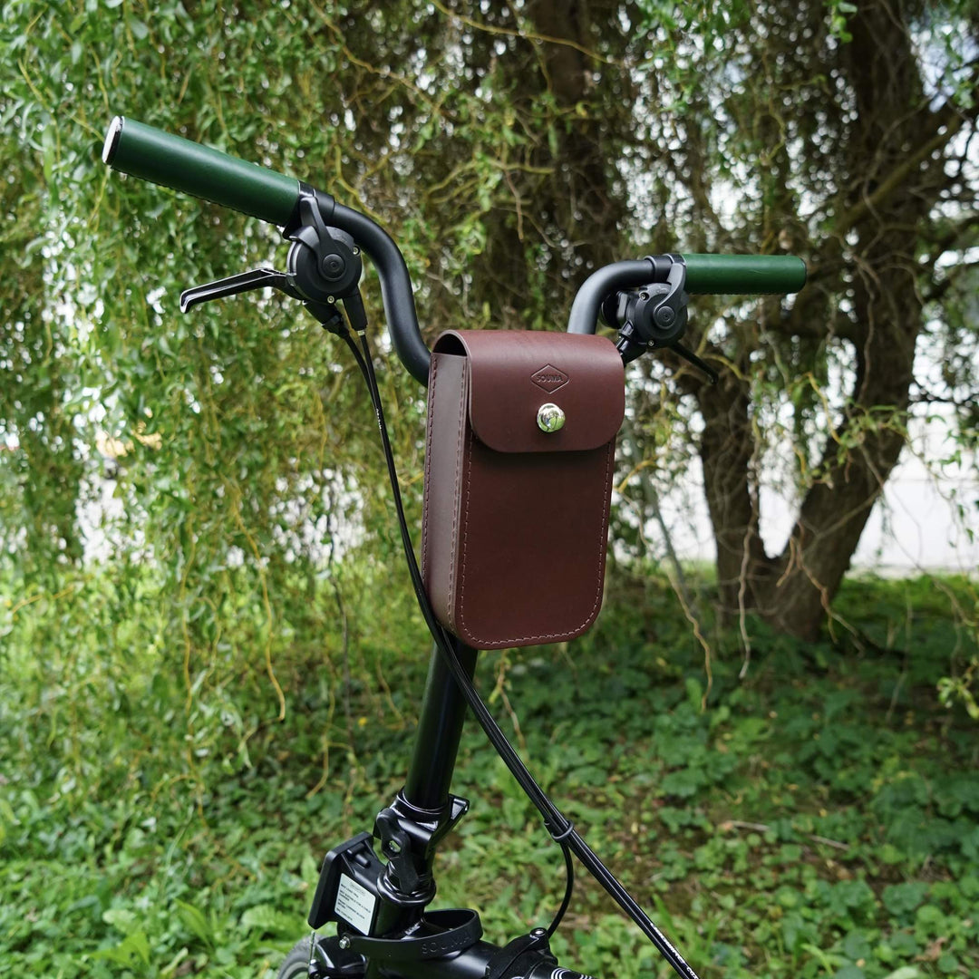 Brown leather pouch on a bicycle handlebar with a natural background