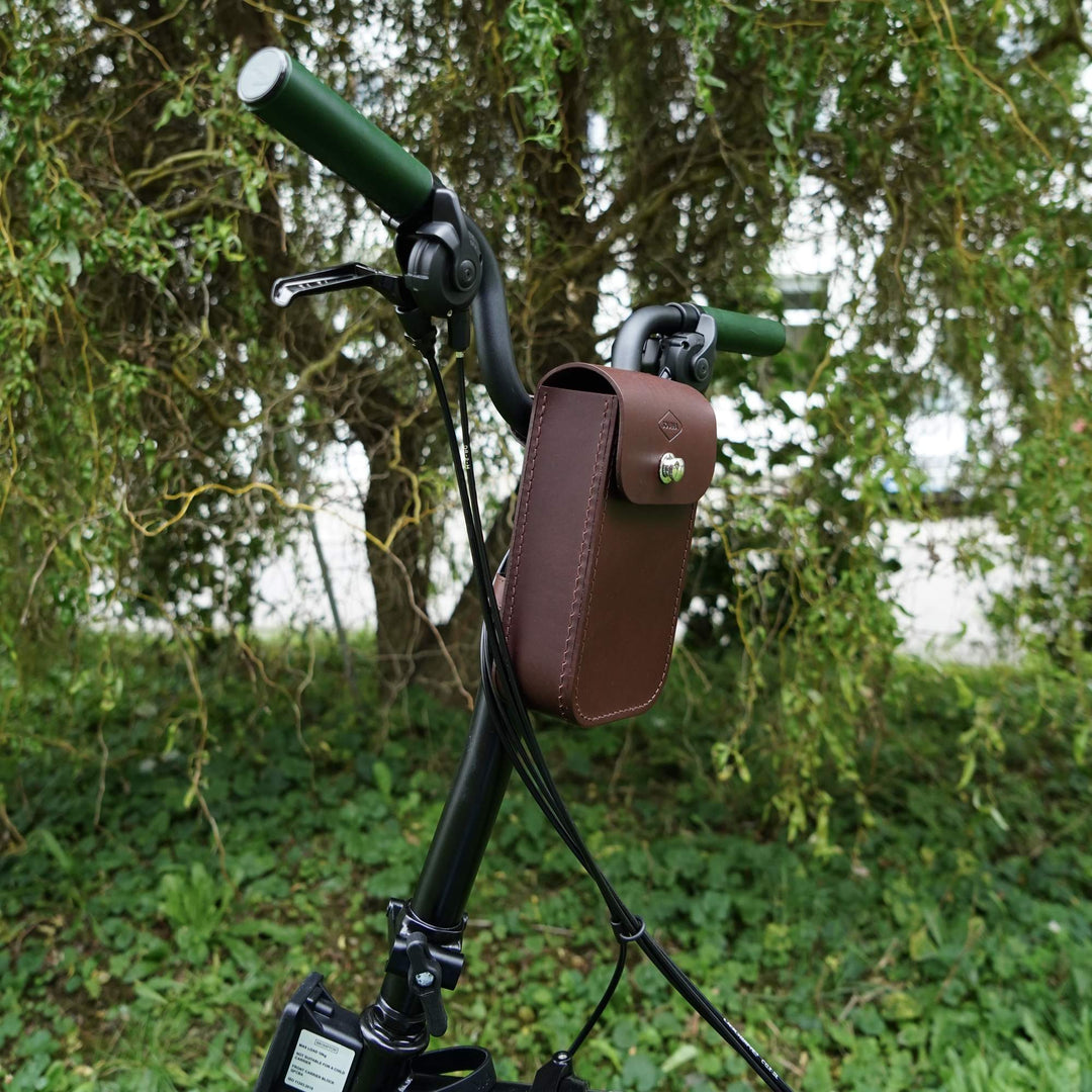 Brown leather bike handlebar bag with a blurred green background sideview
