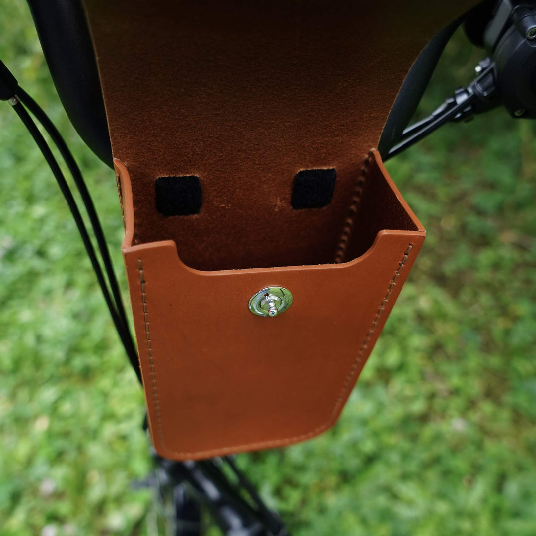 Honey leather handlebar bag attached to a bicycle frame with a blurred green background