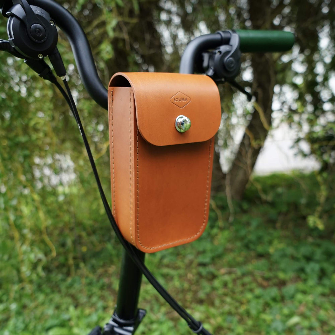 Honey leather pouch attached to a bicycle handlebar with a blurred green background
