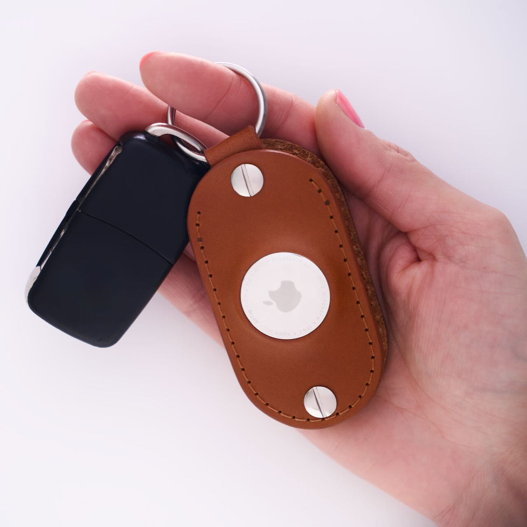 Hand holding a honey leather airtag keychain on a white background