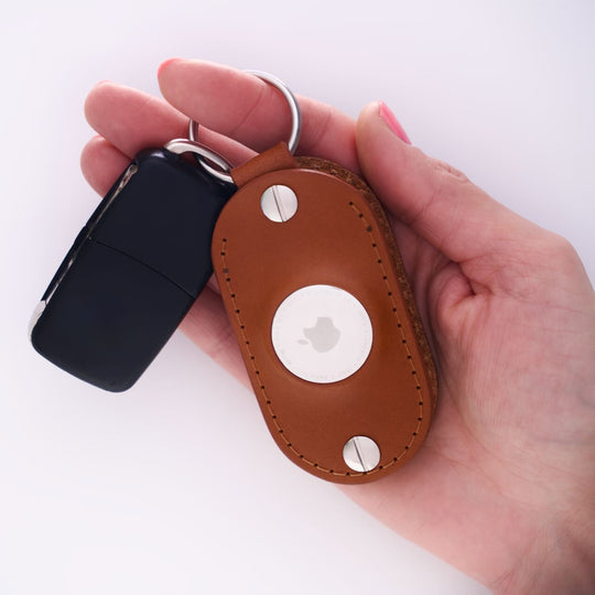 Hand holding a honey leather airtag keychain on a white background